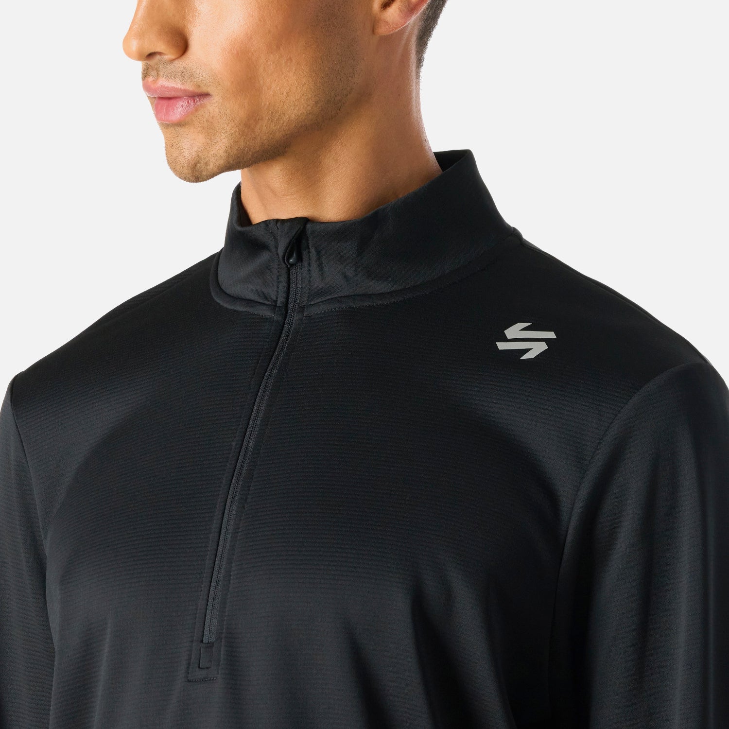 Detalle del logo en el pecho del Polerón Hombre Built To Move 1/4 Zip Midlayer Negro Vulcano, con textura técnica y cierre hasta el pecho para ventilación.