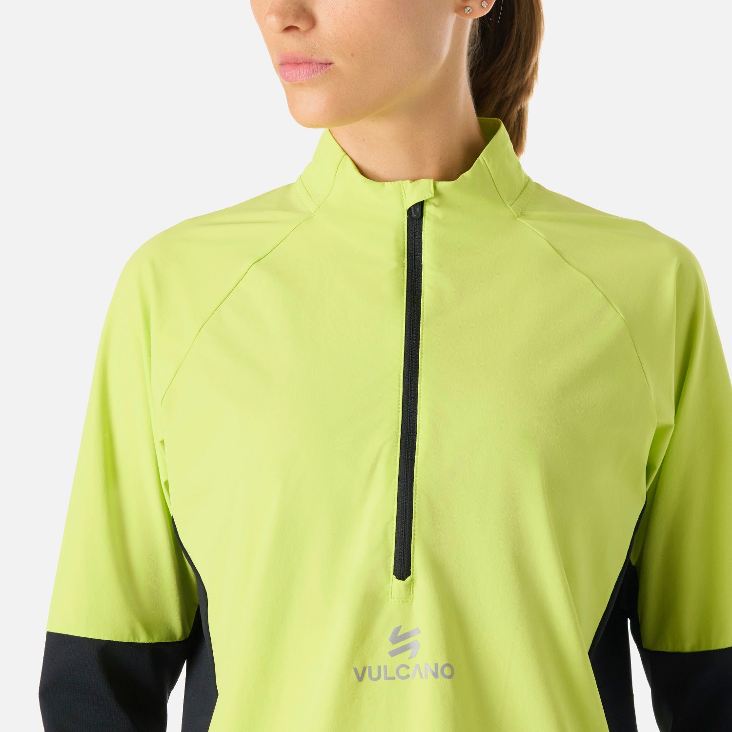 Detalle del cierre frontal y logo Vulcano en el Polerón Mujer Built To Move Pro 1/4 Zip Midlayer Verde Lima, con tela cortaviento ligera.