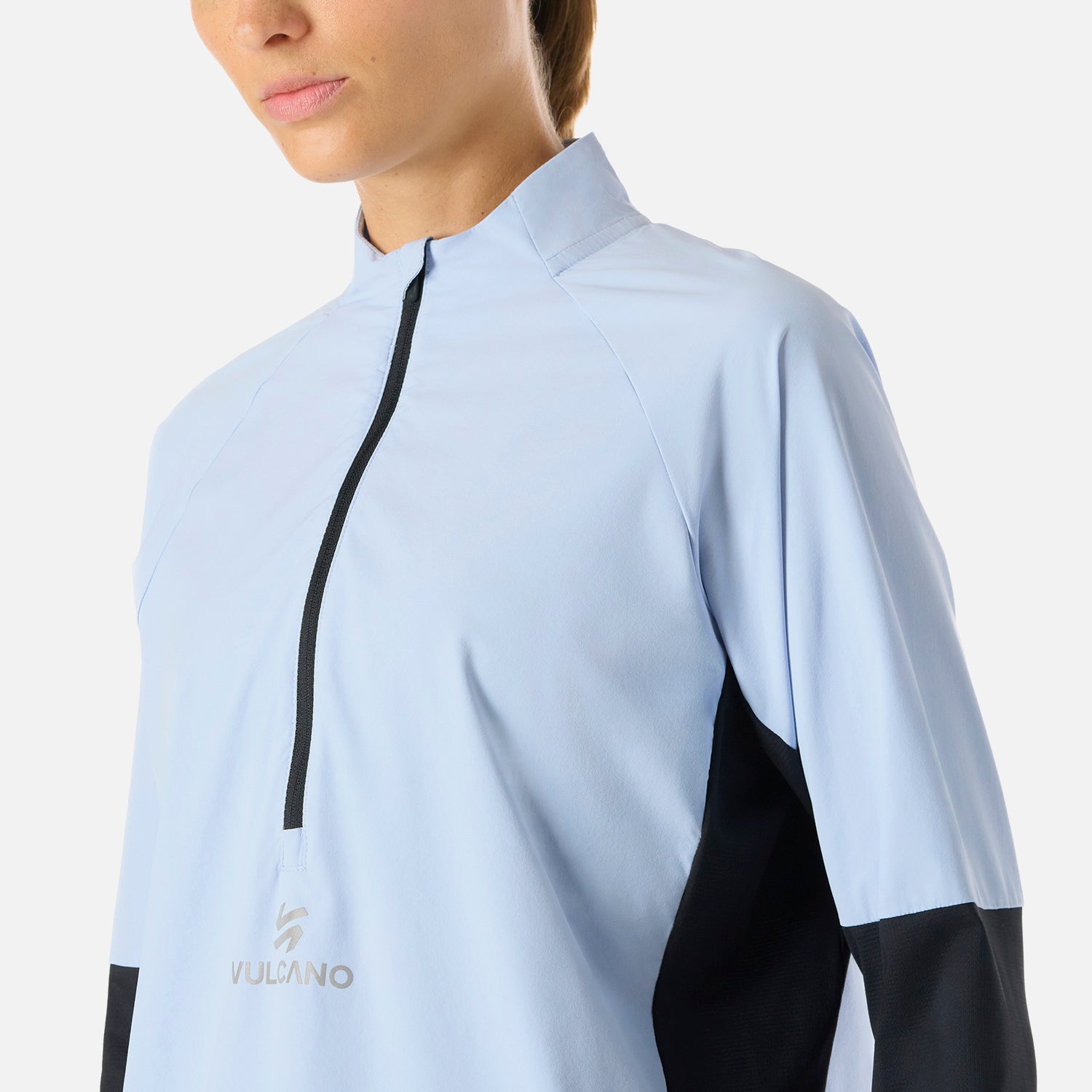 Detalle del cierre frontal y logo Vulcano en el Polerón Mujer Built To Move Pro 1/4 Zip Midlayer Celeste, con tela cortaviento ligera.