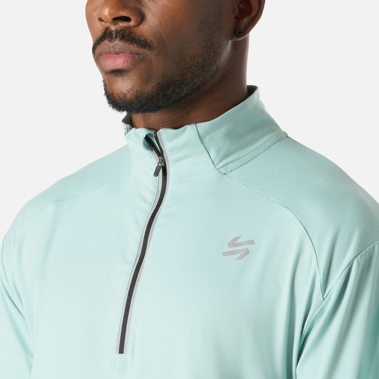 Detalle del cierre y cuello alto del Polerón Hombre Tempo 1/4 Zip Midlayer Jade Vulcano, con logo reflectante para mayor visibilidad en exteriores.